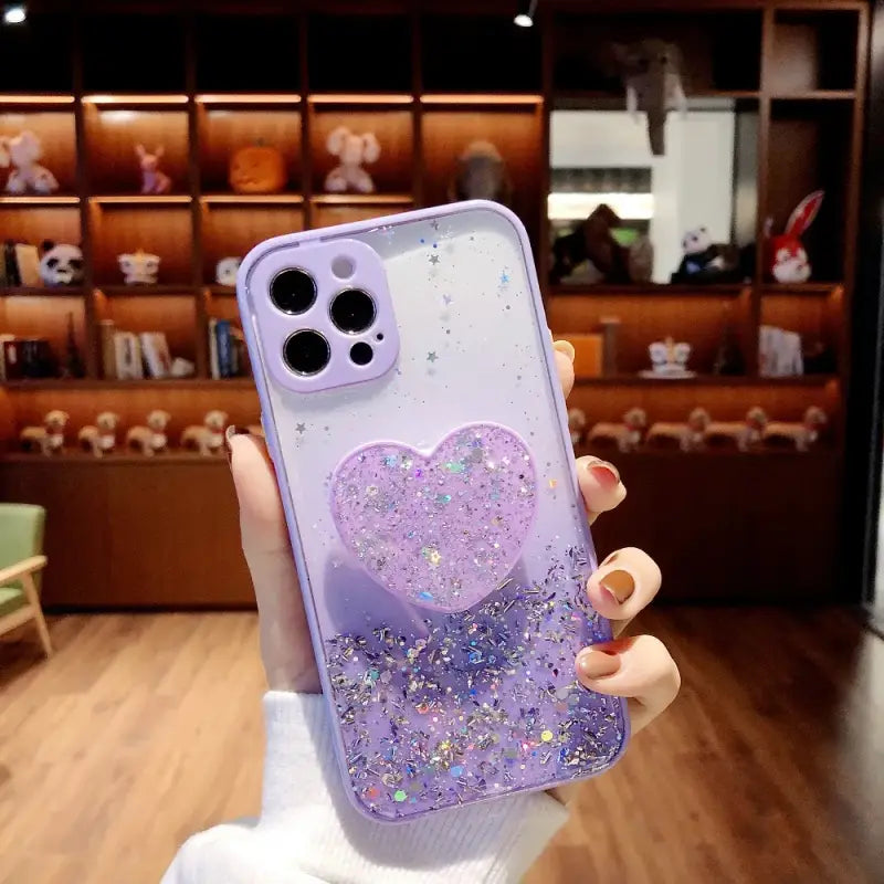 a girl holding up a purple phone case with glitter heart