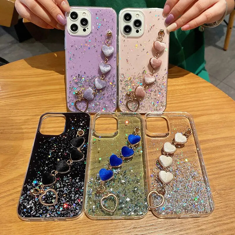 a woman holding up three iphone cases with glitter and heart charms