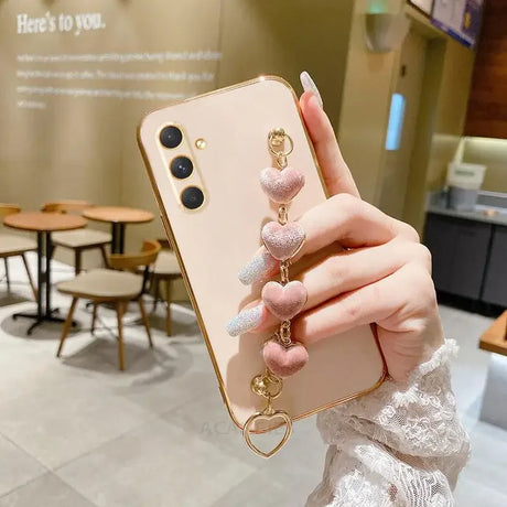 Gold-colored smartphone with a pink heart charm accessory attached.