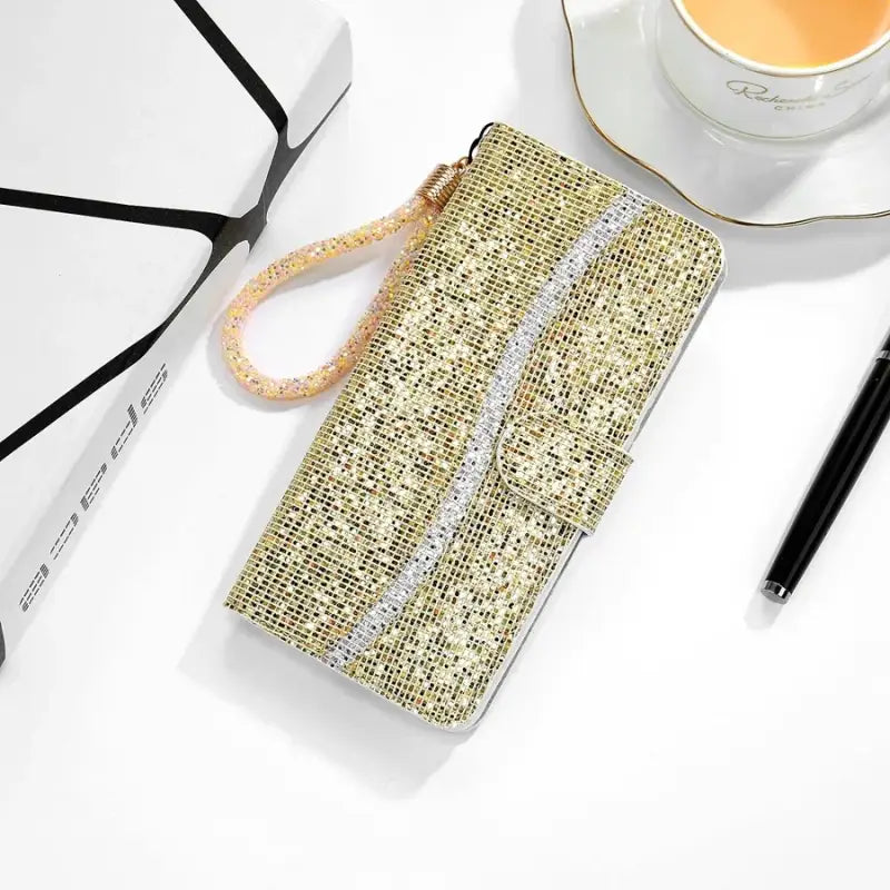 A gold glitter phone case with a cup of coffee and a pen