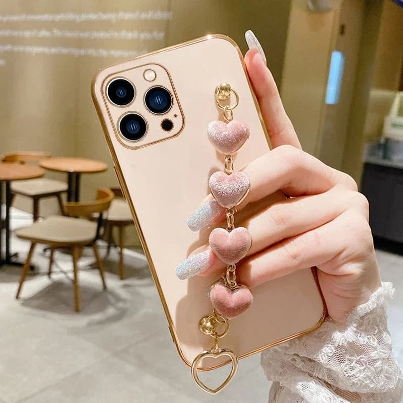 Gold iPhone with a pink heart-shaped charm accessory attached.