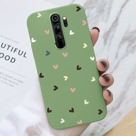 A hand holding a green phone case with hearts on it