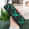 A hand holding a phone case with a green and black pattern