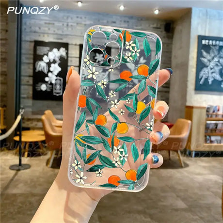 A hand holding a phone case with a painting of oranges and leaves