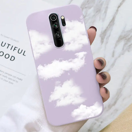 A hand holding a purple phone case with clouds in the sky