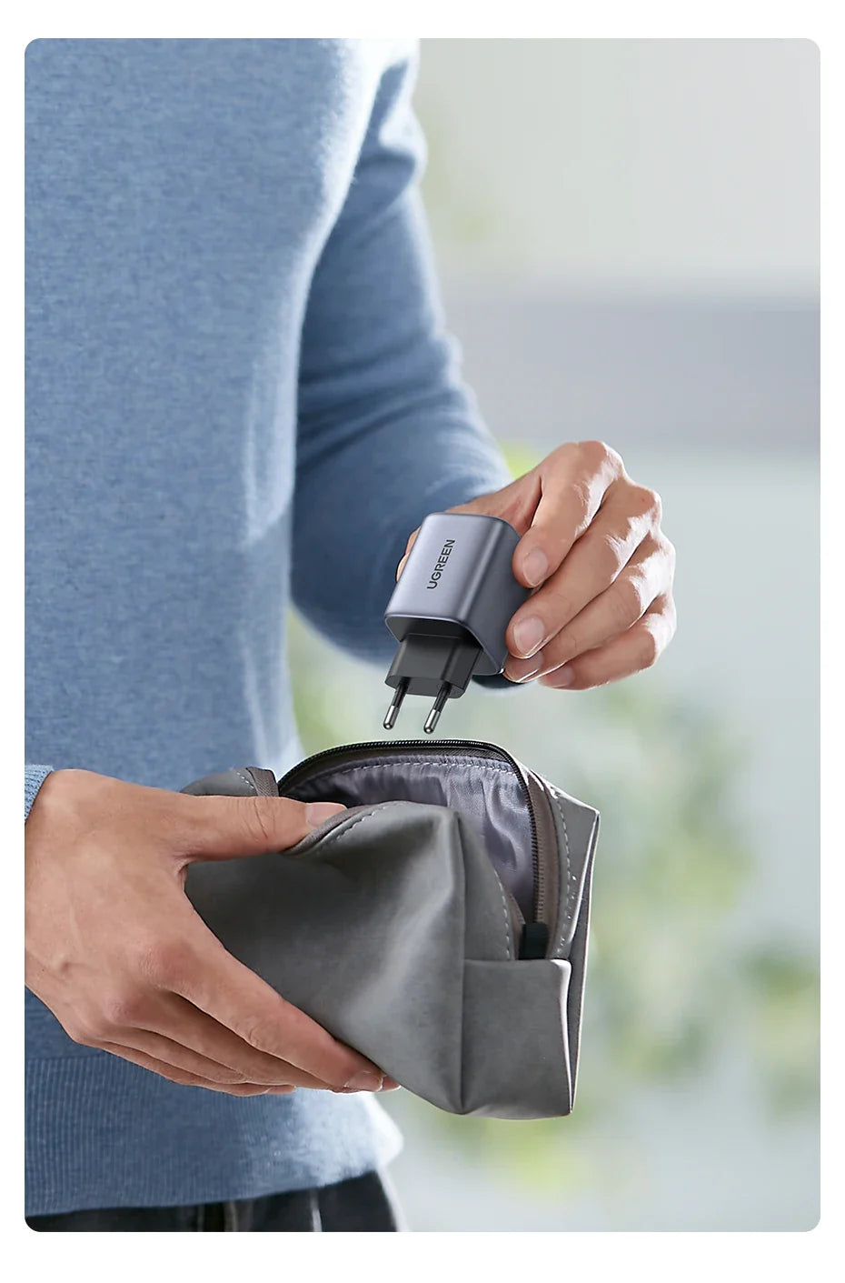 Hands holding a gray travel adapter and placing it into a small pouch or case.