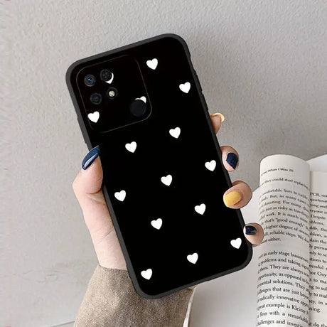 a woman holding a black phone case with white hearts on it