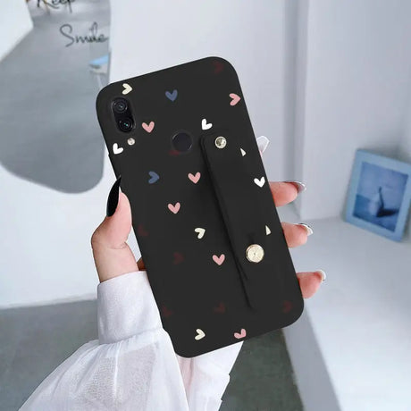 a woman holding up a black phone case with hearts on it