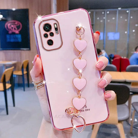 a woman holding a pink phone case with heart charms