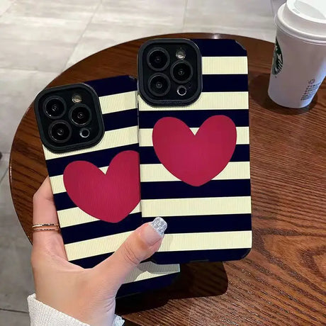 a woman holding up two iphone cases with hearts on them