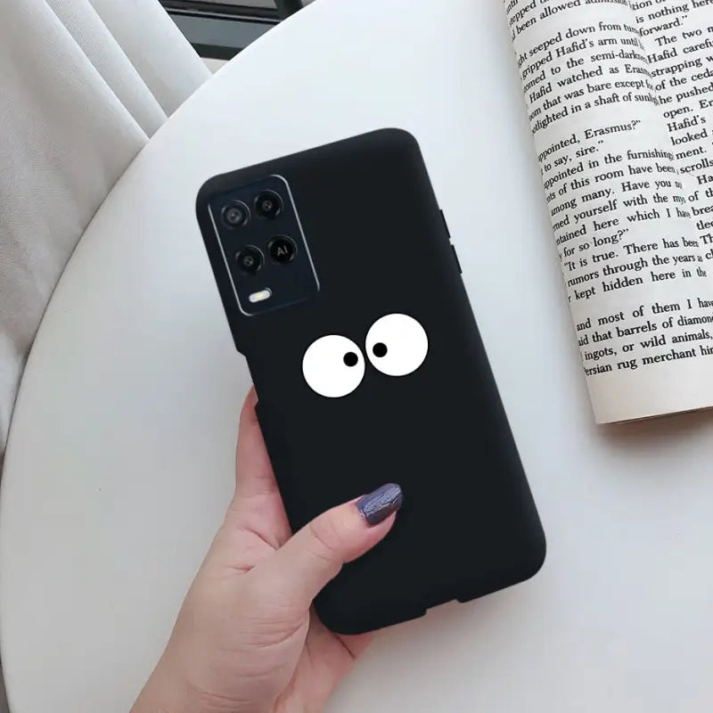 a hand holding a black phone case with a cartoon face on it