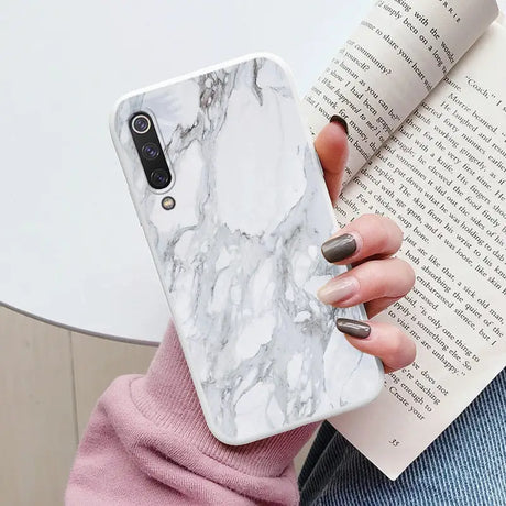 a woman holding a book and a white marble phone case