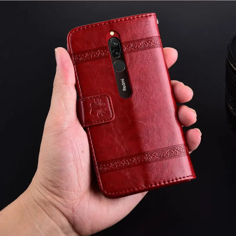 a hand holding a red leather case with a camera in the background