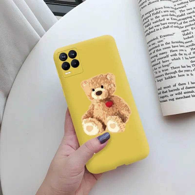 a person holding a yellow phone case with a teddy bear