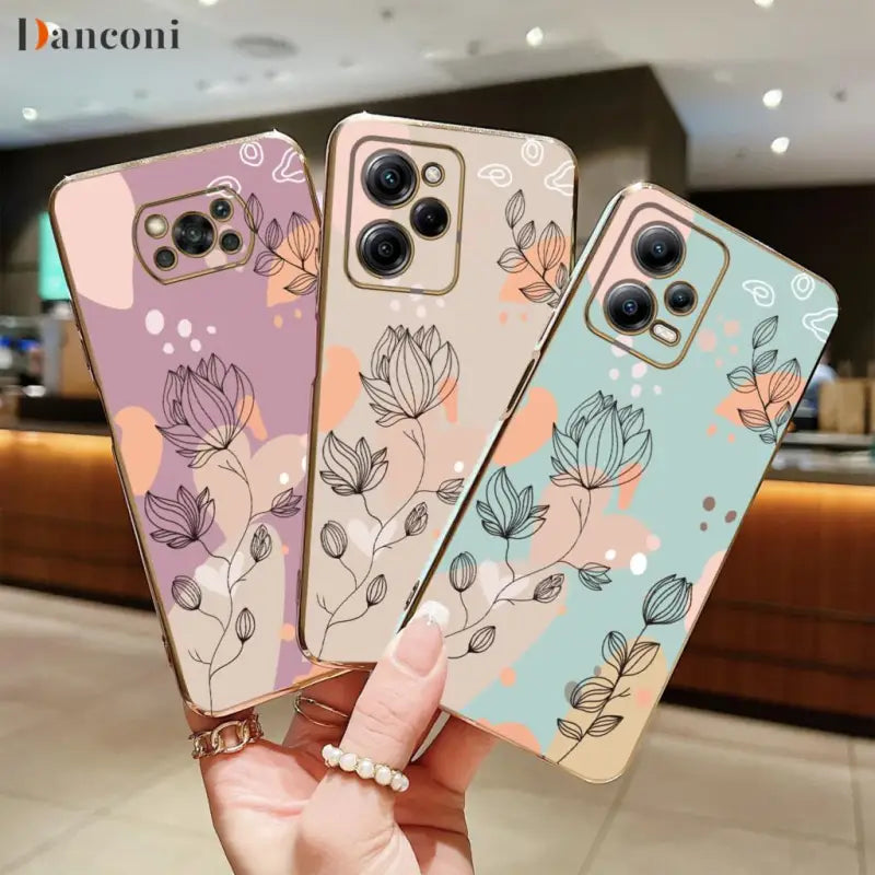 a woman holding three iphone cases with flowers on them