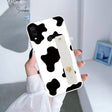 a woman holding a phone case with a cow print