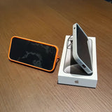 IPhone in its retail box alongside an orange-rimmed portable speaker or device case.