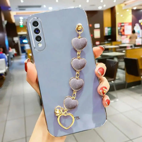 Lavender smartphone case with a dangling heart-shaped charm accessory.