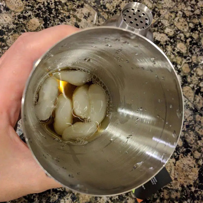 a hand holding a metal cup filled with ice