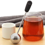a glass tea pot with a tea strainer and a cup of tea