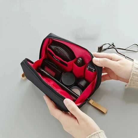 Makeup bag with red interior being opened to reveal cosmetic products inside.