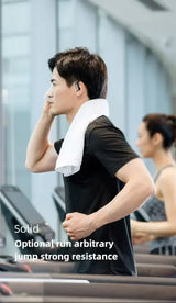 Man wearing a black t-shirt and white towel on a treadmill with an earbud.