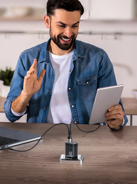 Smiling man in a denim shirt holding a tablet and gesturing enthusiastically.