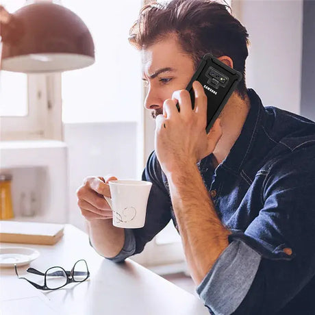 A man is talking on the phone while drinking coffee