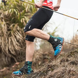 a man in a red shirt and black shorts is walking up a hill with a stick