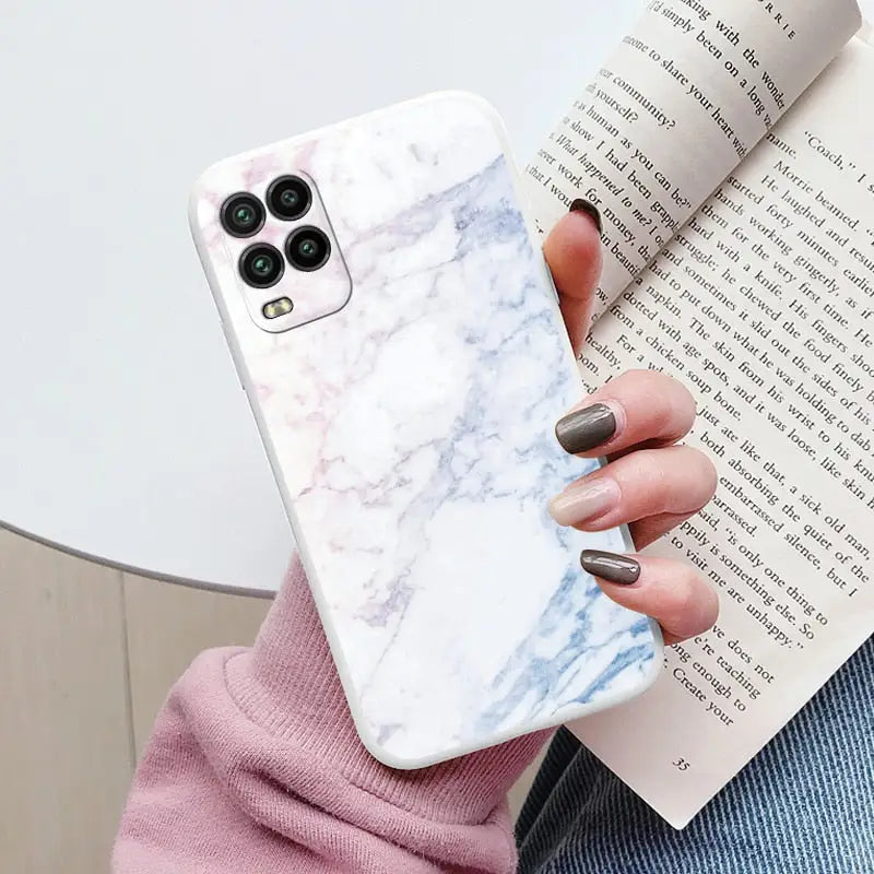 a woman holding a book and a white marble phone case