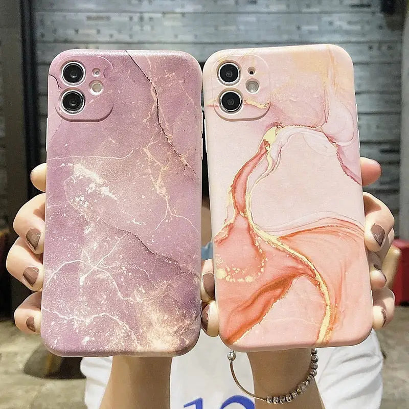 a woman holding two iphone cases with pink marble