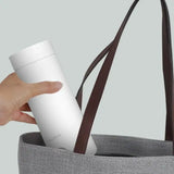 a hand holding a white cup in a gray bag