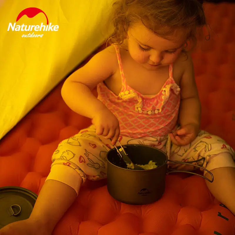 a little girl sitting on a bed with a pot of food