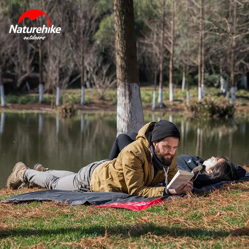 a man and woman laying on the grass in front of a lake