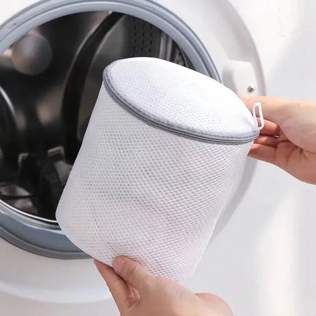 a hand is holding a white mesh bag over a washing machine