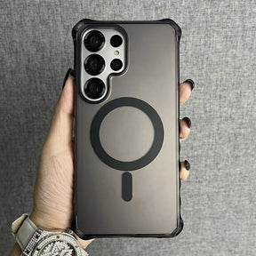 A person holding a dark, translucent phone case with a black MagSafe ring and an elongated ’I’ shape below it, featuring a prominent camera cutout for multiple lenses and corner bumper protection.