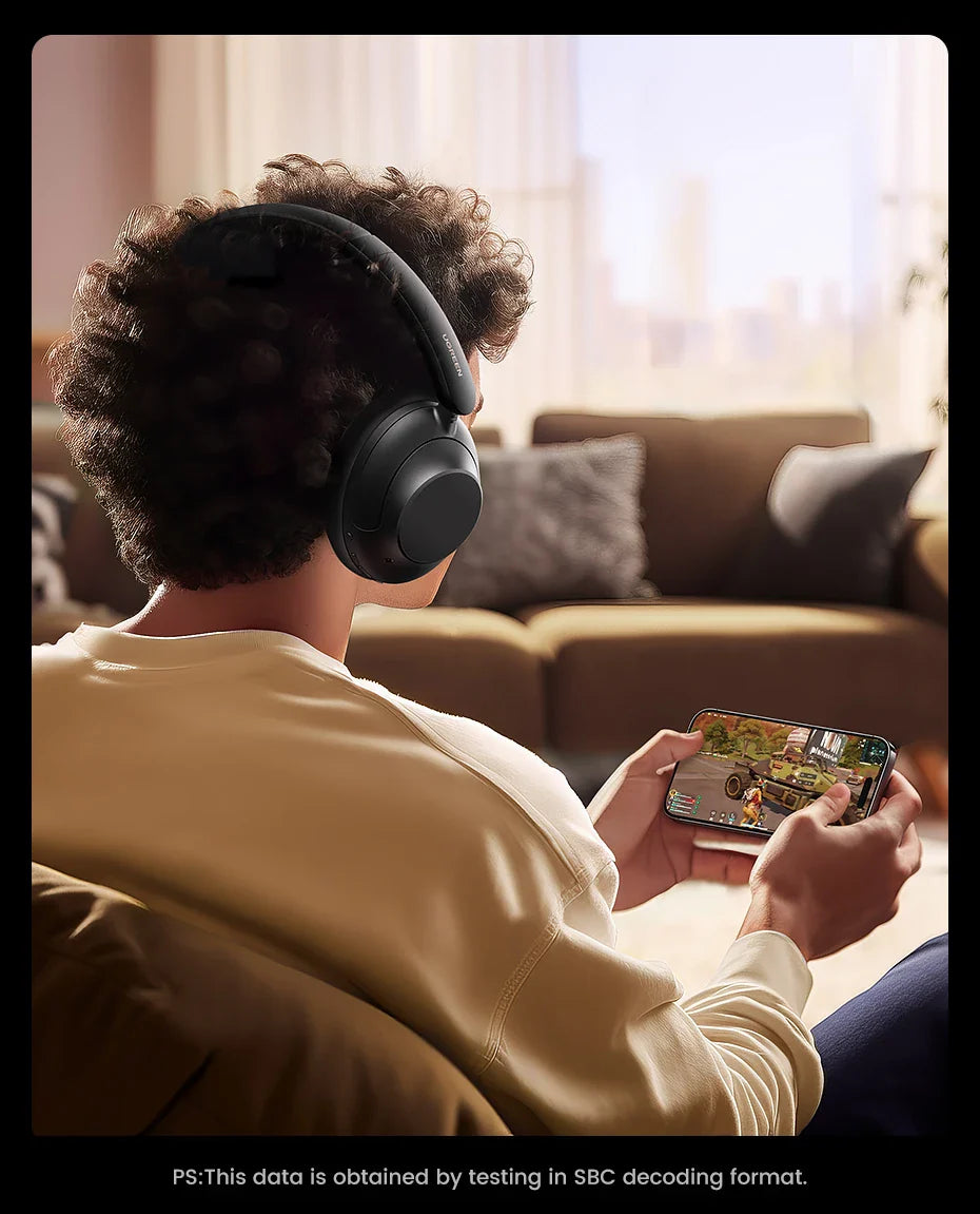 Person wearing headphones while playing a handheld gaming device.