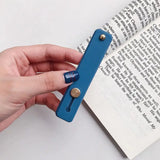 a hand holding a blue bookmark over a book