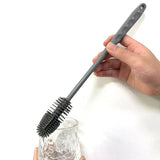 a hand holding a black brush with a glass of water