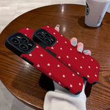 a woman holding a red phone case with white hearts on it