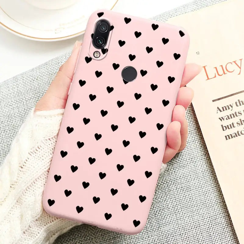 a woman holding a pink phone case with black hearts on it