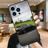 a person holding up a phone case with a car in the background