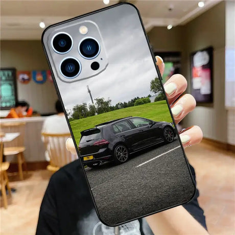 A person holding up a phone case with a car in the background