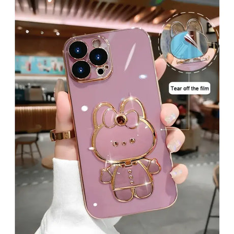 A person holding a pink phone case with a gold hello kitty