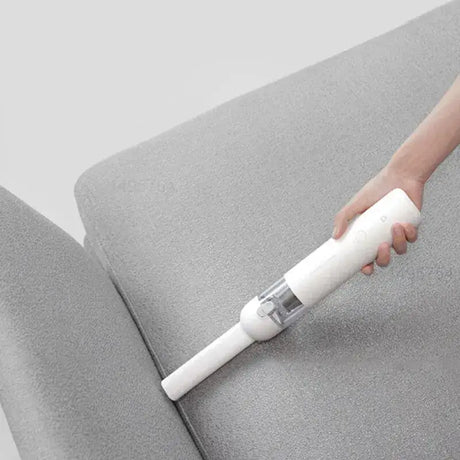 A person using a vacuum to clean a couch