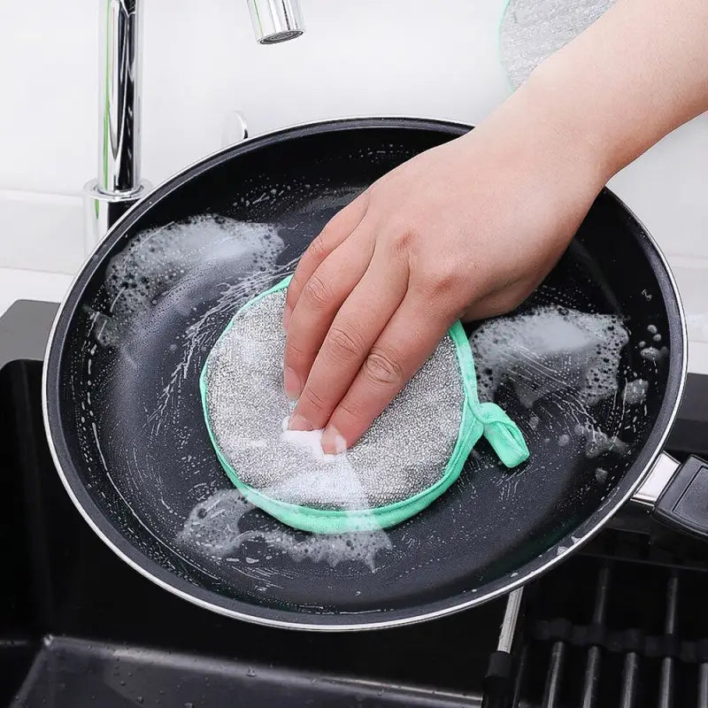 a person is washing a pan with a green sponge