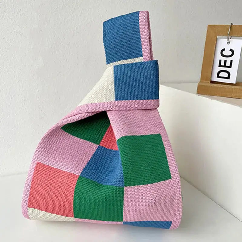 a pink and blue knitted bag sitting on a white table