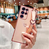 Pink phone case with a heart design and strap.