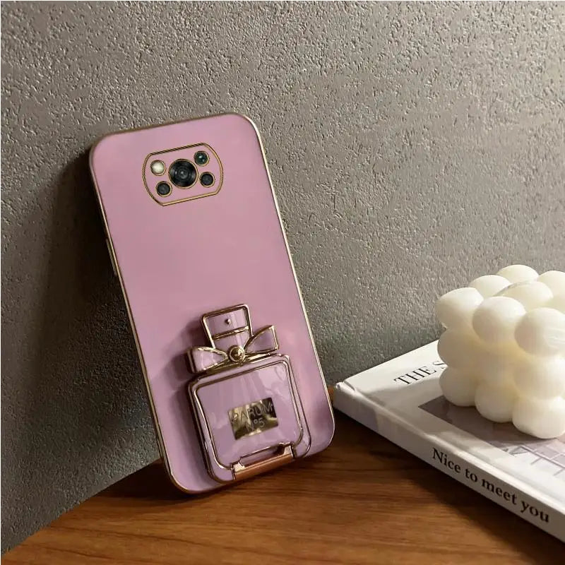 a pink phone case with a perfume bottle on top