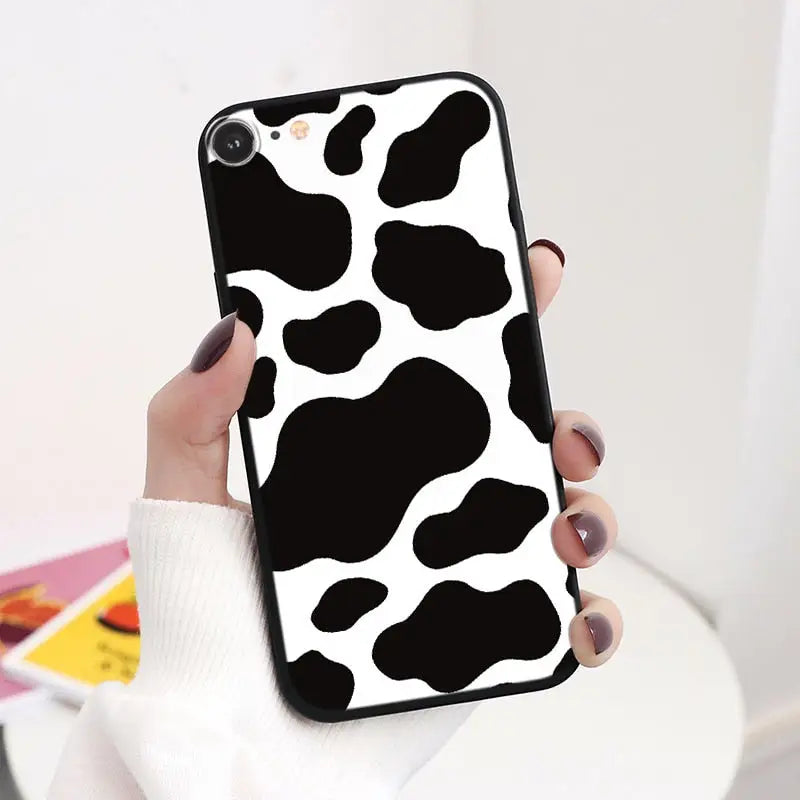 a woman holding a phone case with a cow print